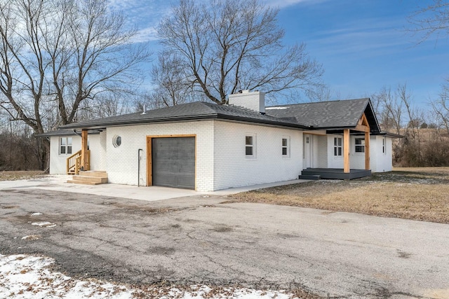 single story home with a shingled roof, brick siding, a chimney, and an attached garage