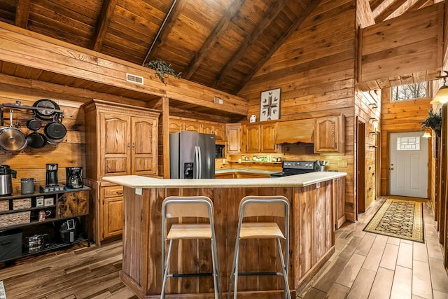 kitchen featuring wooden walls, light countertops, electric stove, stainless steel fridge with ice dispenser, and a center island with sink