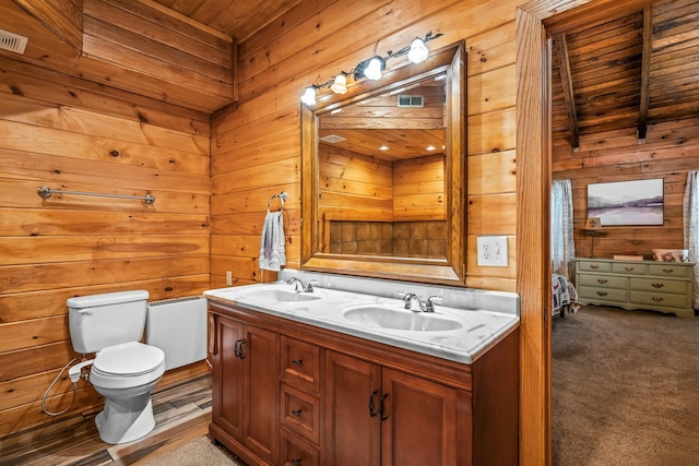 bathroom featuring double vanity, wood walls, toilet, and a sink