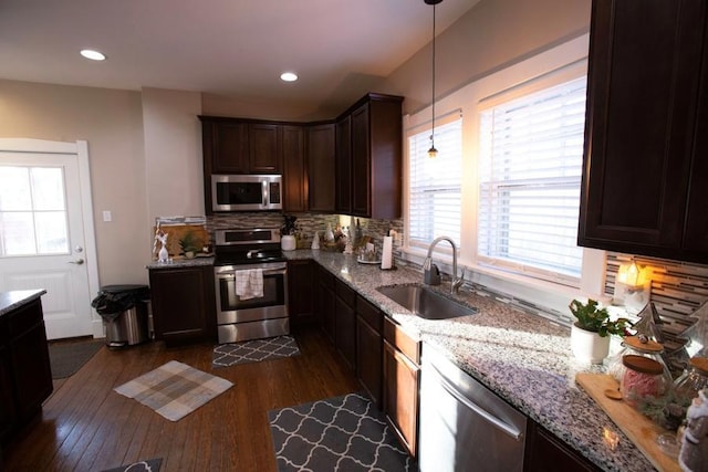 kitchen featuring light stone counters, decorative light fixtures, appliances with stainless steel finishes, dark wood-type flooring, and a sink