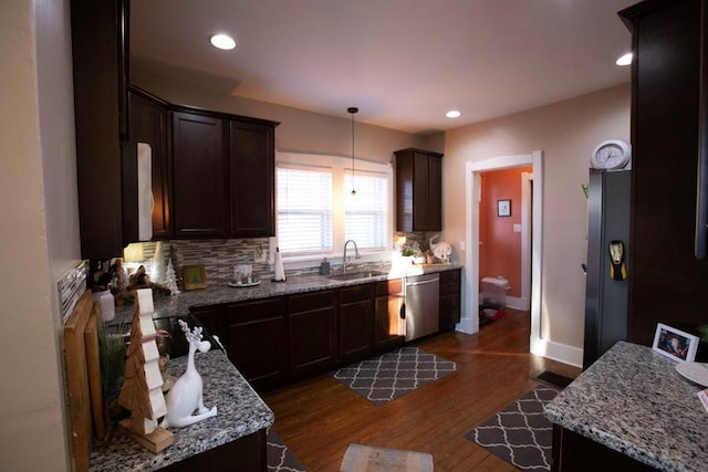 kitchen with light stone counters, a sink, dark brown cabinets, dishwasher, and pendant lighting