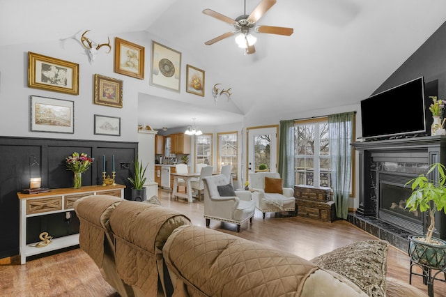 living area with ceiling fan with notable chandelier, high vaulted ceiling, a high end fireplace, and light wood-style flooring