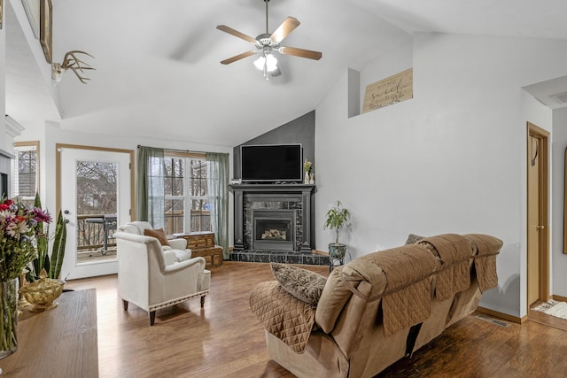 living area with ceiling fan, high vaulted ceiling, a tiled fireplace, and wood finished floors