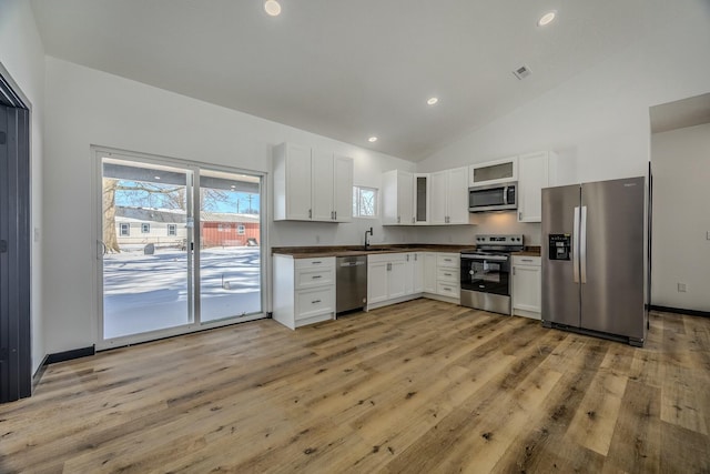 kitchen with light wood finished floors, white cabinets, glass insert cabinets, appliances with stainless steel finishes, and a sink