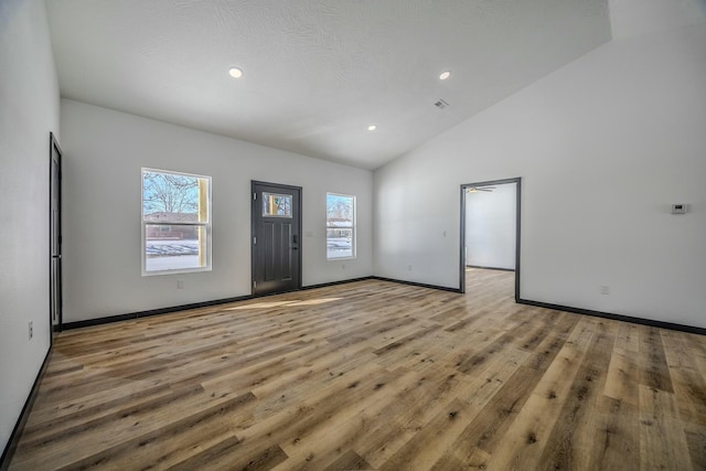 empty room featuring light wood finished floors, baseboards, high vaulted ceiling, and recessed lighting