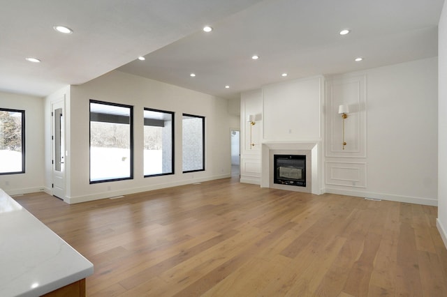 unfurnished living room with baseboards, light wood-type flooring, a glass covered fireplace, and recessed lighting