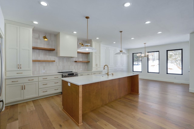 kitchen with a large island, open shelves, light countertops, white cabinetry, and a sink