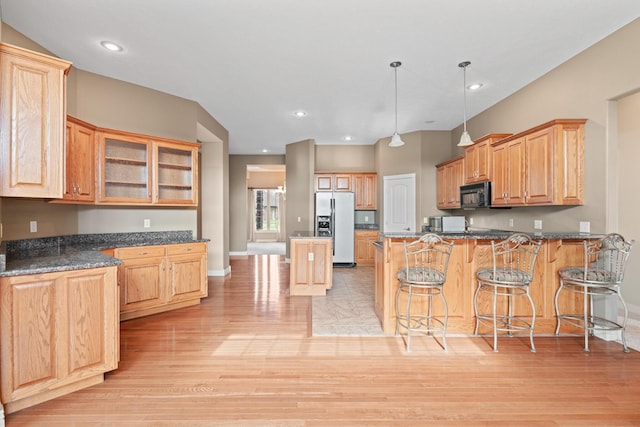 kitchen with pendant lighting, stainless steel fridge with ice dispenser, glass insert cabinets, black microwave, and a kitchen breakfast bar