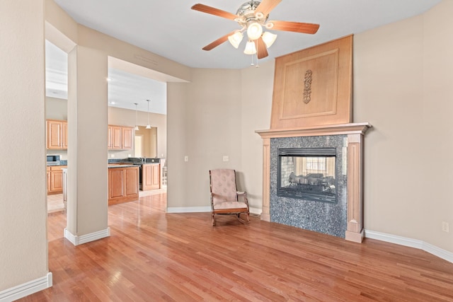 unfurnished room featuring light wood-style flooring, baseboards, a ceiling fan, and a multi sided fireplace