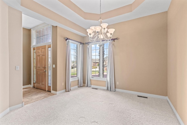 unfurnished room with a tray ceiling, baseboards, a notable chandelier, and light colored carpet