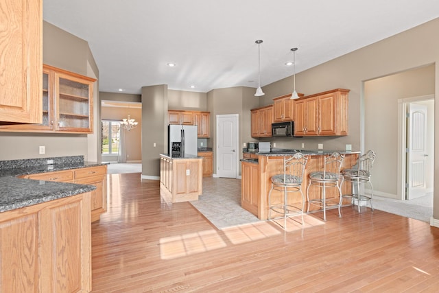 kitchen featuring decorative light fixtures, a kitchen bar, glass insert cabinets, black microwave, and stainless steel fridge with ice dispenser