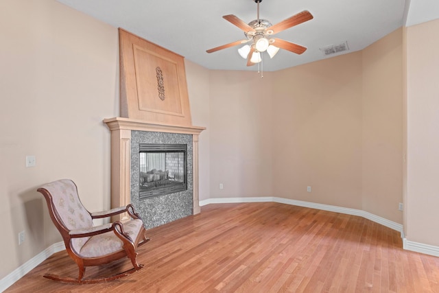 sitting room with visible vents, light wood-style flooring, a ceiling fan, a tile fireplace, and baseboards