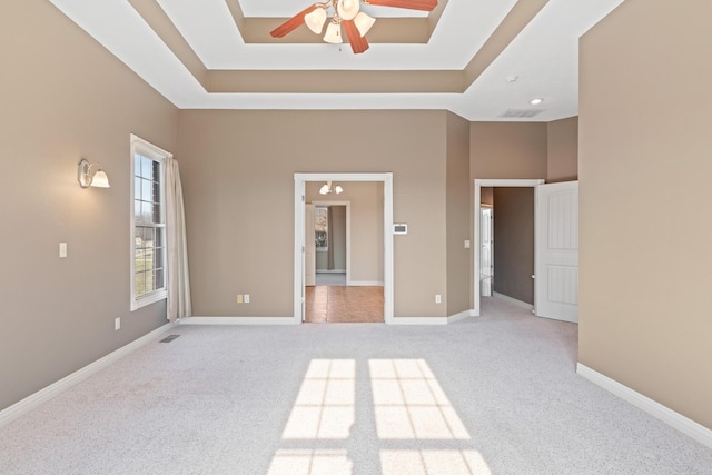 unfurnished bedroom with light carpet, a towering ceiling, baseboards, and a raised ceiling