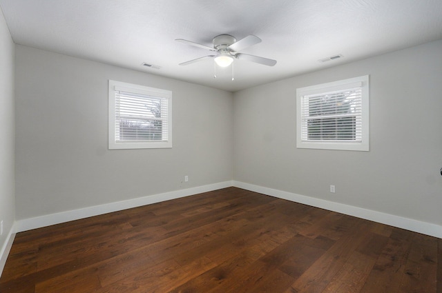 empty room with a ceiling fan, dark wood-style flooring, visible vents, and baseboards