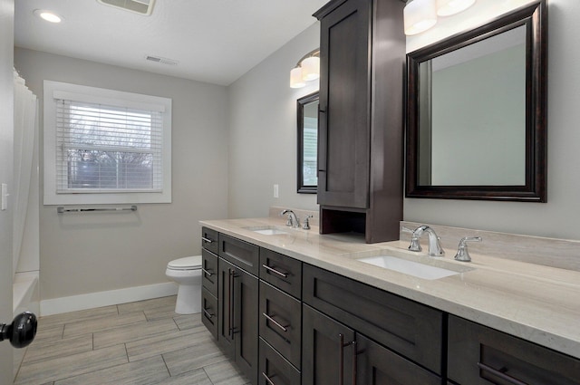 bathroom with toilet, double vanity, baseboards, and a sink