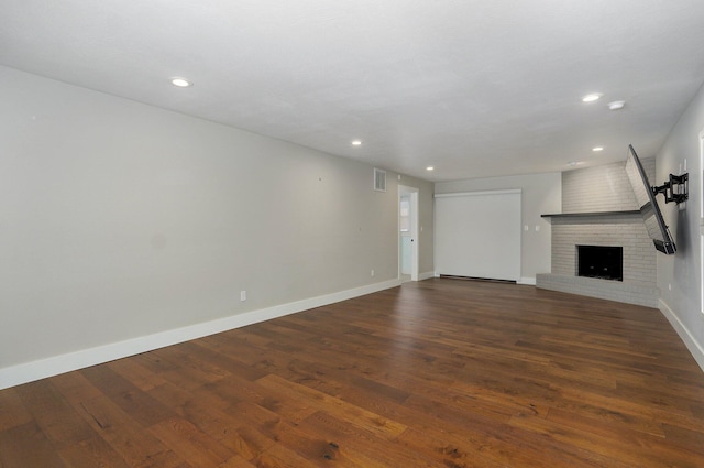 unfurnished living room with recessed lighting, visible vents, baseboards, a brick fireplace, and dark wood-style floors