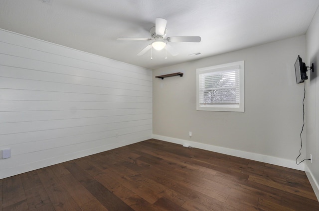 empty room featuring dark wood-style floors, visible vents, a ceiling fan, and baseboards