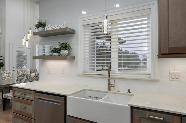 kitchen featuring light stone counters, pendant lighting, open shelves, a sink, and dishwasher