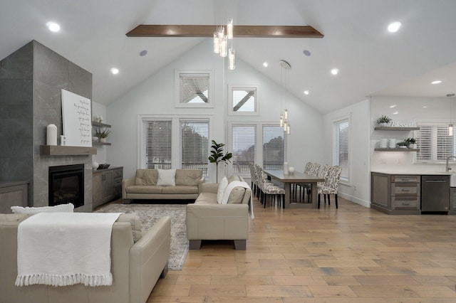 living room with light wood-type flooring, a tile fireplace, beamed ceiling, and high vaulted ceiling