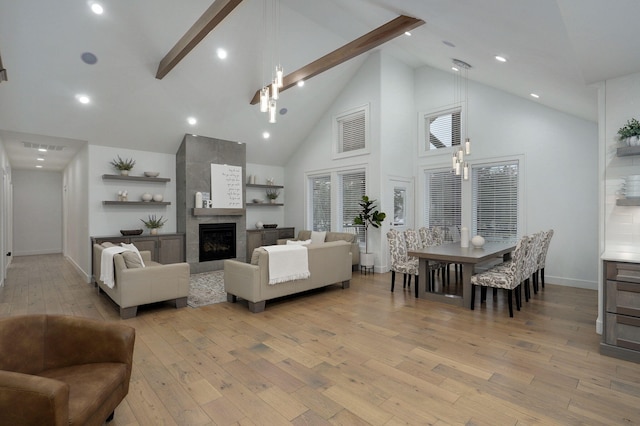 living area featuring beam ceiling, light wood finished floors, high vaulted ceiling, a tile fireplace, and baseboards