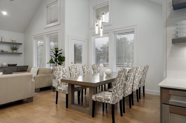 dining space featuring light wood-style floors, baseboards, and high vaulted ceiling