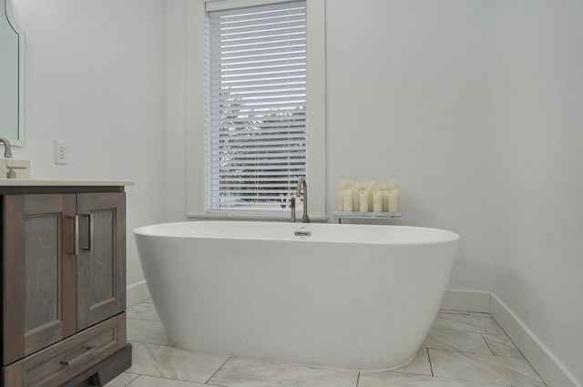 bathroom featuring marble finish floor, plenty of natural light, a freestanding tub, and vanity