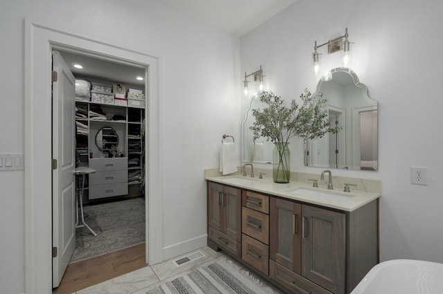 full bathroom with double vanity, a spacious closet, visible vents, and a sink