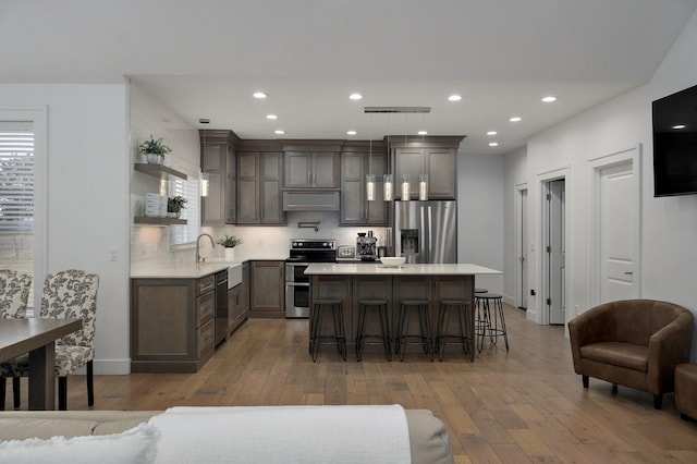 kitchen featuring a center island, light countertops, appliances with stainless steel finishes, light wood-style floors, and a kitchen breakfast bar