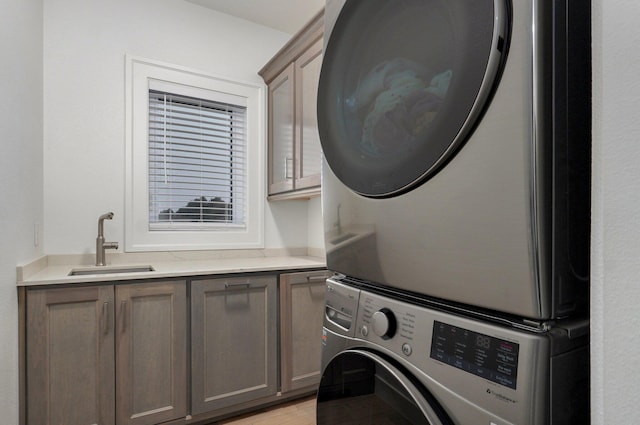 washroom featuring light wood-style floors, stacked washer and clothes dryer, cabinet space, and a sink