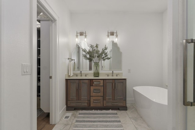 bathroom with a walk in closet, a sink, a freestanding bath, and double vanity