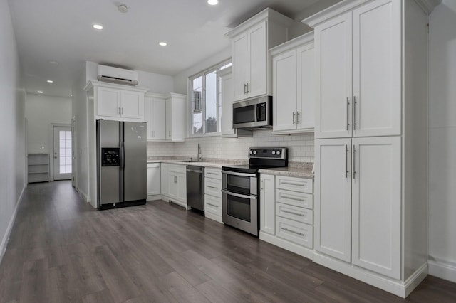 kitchen featuring dark wood finished floors, decorative backsplash, appliances with stainless steel finishes, white cabinetry, and a wall mounted air conditioner