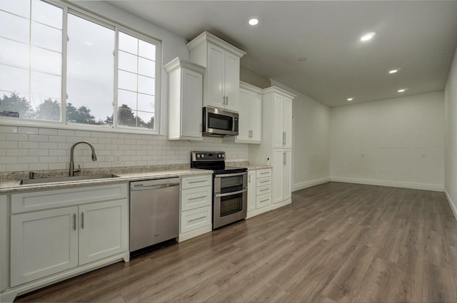 kitchen featuring stainless steel appliances, tasteful backsplash, white cabinetry, a sink, and light wood-type flooring