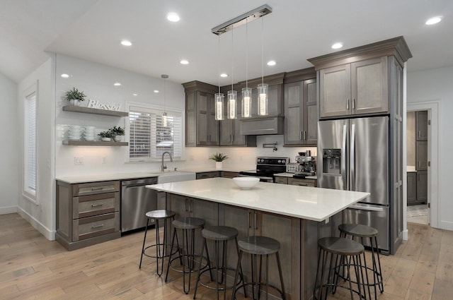 kitchen featuring decorative light fixtures, stainless steel appliances, light countertops, open shelves, and a sink