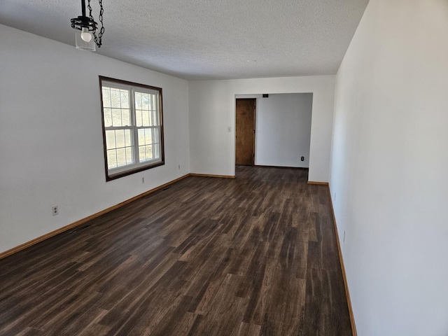 empty room with a textured ceiling, dark wood finished floors, and baseboards