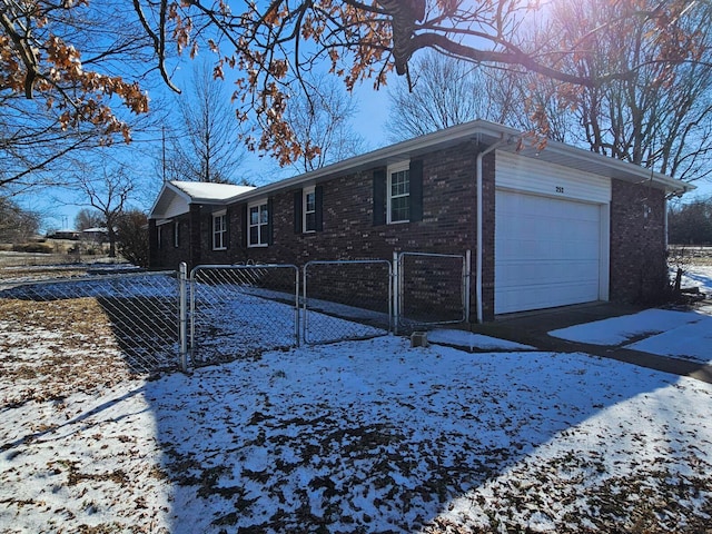 snow covered property with a garage, brick siding, and fence