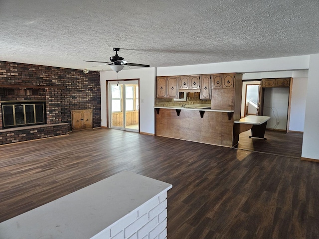 unfurnished living room featuring a textured ceiling, dark wood-type flooring, a brick fireplace, and a ceiling fan