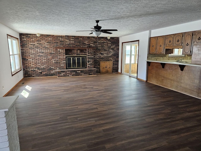 unfurnished living room featuring dark wood-style floors, brick wall, ceiling fan, a textured ceiling, and a brick fireplace