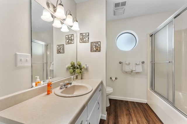 full bathroom with visible vents, toilet, wood finished floors, combined bath / shower with glass door, and vanity