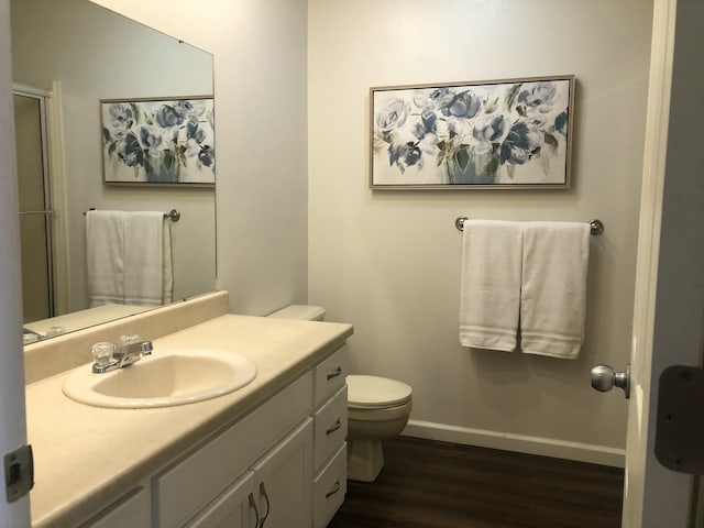 bathroom featuring toilet, wood finished floors, vanity, baseboards, and a shower with door