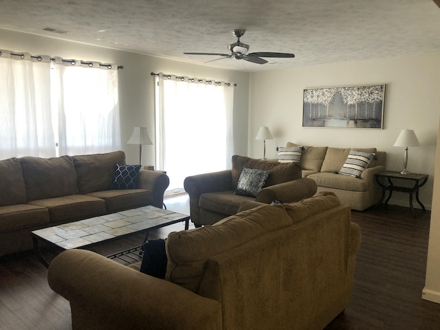 living room featuring a textured ceiling, dark wood finished floors, visible vents, and a ceiling fan