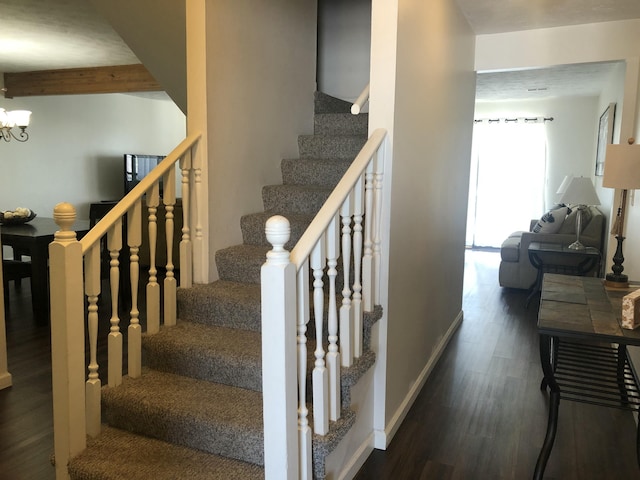 stairway featuring a chandelier, beam ceiling, baseboards, and wood finished floors