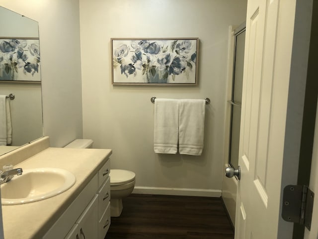 bathroom featuring baseboards, toilet, a shower with door, wood finished floors, and vanity