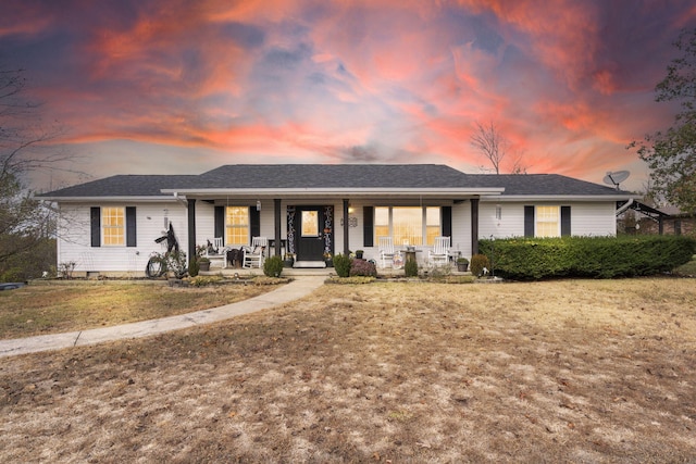 single story home featuring covered porch, a shingled roof, and a lawn