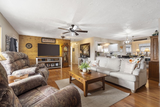 living area with ceiling fan, a textured ceiling, and wood finished floors