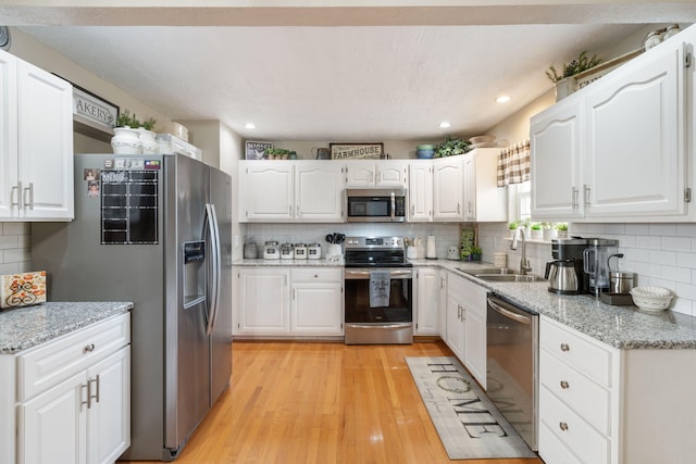 kitchen featuring appliances with stainless steel finishes, white cabinets, a sink, and light wood-style flooring