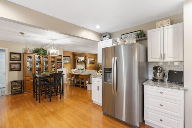 kitchen with light wood-style floors, white cabinets, stainless steel refrigerator with ice dispenser, light stone countertops, and decorative light fixtures