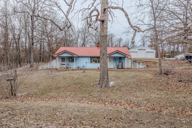 view of front of property with a detached garage, a porch, metal roof, an outdoor structure, and a front lawn