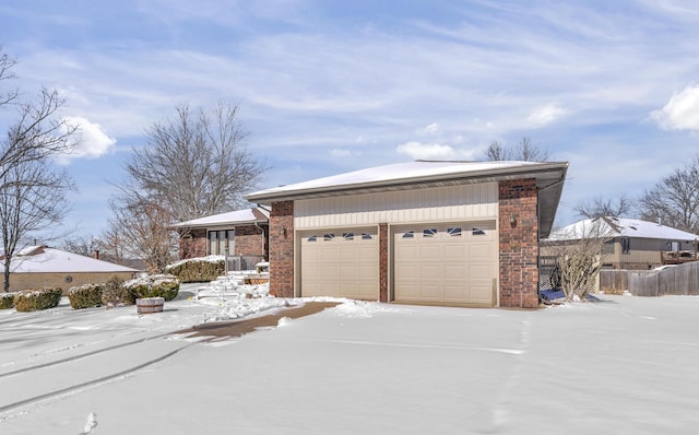 view of snow covered exterior with brick siding, a garage, and fence