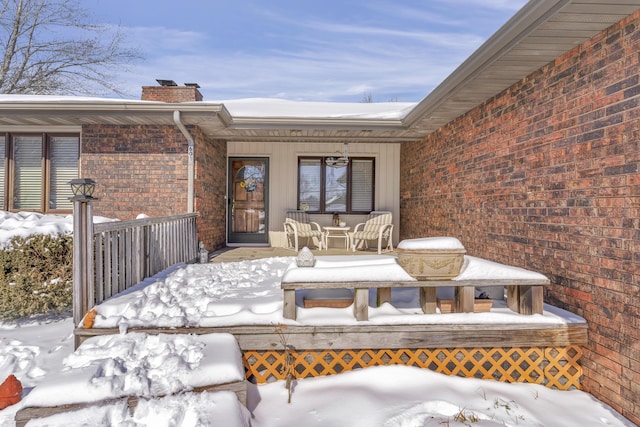 snow covered property entrance with covered porch, brick siding, and a chimney