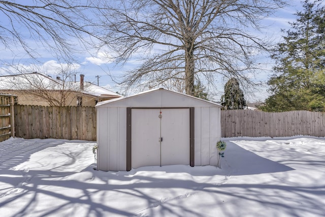 snow covered structure with a storage shed, a fenced backyard, and an outdoor structure